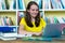 Smiling german female student learning with book and computer at desk