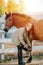 Smiling ginger girl cleaning horse`s hoof with a pick. Smiling at the camera