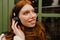 Smiling ginger woman listening music with headphones while standing outdoors