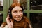Smiling ginger woman listening music with headphones while standing outdoors