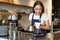 Smiling girl barista, asian bartender pouring water from kettle, brewing filter coffee in cafe behind counter, wearing