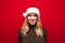 Smiling girl in a Christmas hat and a warm sweater stands on a red background and smacks of the camera. Happy lady in santa claus