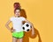 Smiling girl with colorful dreadlocks hairstyle in sportswear standing with soccer ball in hand