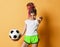 Smiling girl with colorful dreadlocks hairstyle in sportswear standing with soccer ball in hand and pointing at camera