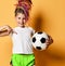 Smiling girl with dreadlocks in sportswear standing with soccer ball in hand pointing at copy space on her white t-shirt