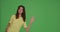 Smiling girl greeting, wave hand say hello or bye to subscribers, peek out on chromakey green background with copy space