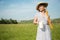 Smiling girl in a hat and dress holds bread and a carafe of milk in her hands. Standing on a lawn against the sky natural food