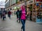 A smiling girl in headphones walks between small street shops in a shopping center in a city near the metro. Passers-by rush about