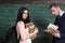 Smiling girl with heap of books standing in front of her stylish young professor concentrated on reading