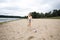 Smiling girl with long blond hair and long legs runs along the beach towards a soccer ball