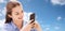 Smiling girl messaging on smartphone over blue sky