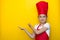 Smiling girl in a red chef`s suit points with both hands to a copy space on a yellow background