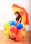 Smiling girl with red and yellow umbrella behind inflating balloons