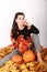 Smiling girl sitting on autumn leaves with pumpkins and flowers