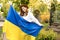 Smiling girl standing in Ukrainian flag worried about war. Young woman is feeling emotional pain after reading the news
