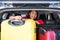 Smiling girl in suv car with suitcase on boot