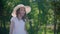 Smiling girl teenager with curly hair and hat twisting in green park at sunny day. Happy curly girl in white hat