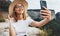 Smiling girl traveler in hat communicates by video call on mobile phone ralax on top of mountain landscape, female hipster tourist