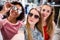 Smiling girlfriends wearing stylish sunglasses having fun time taking selfie with mobile phone while doing shopping in