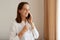 Smiling good looking woman with dark hair wearing white cotton shirt having conversation via smart phone, having positive facial