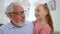 Smiling grandfather looking at granddaughter. Girl hugging senior man in room