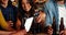 Smiling group of friends using digital tablet while having bottle of beer