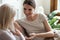 Smiling grownup daughter and mature mom relax talking at home