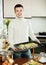 Smiling guy cooking trout fish in roasting pan