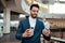 Smiling handsome millennial islamic guy with beard in suit with cup of coffee takeaway looks at phone