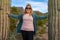 Smiling happy blonde woman stands between two large saguaro cactus, touching each of them