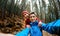 Smiling happy couple hikers with backpacks making selfie on the dark dramatic mossy woods background