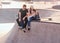 Smiling happy couple of students are sitting at skatepark with their longboards