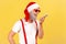 Smiling happy grey bearded man in red santa claus hat and stylish glasses holding smartphone near mouth talking to voice assistant