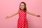 Smiling happy little charming girl with outstretched hands in a pink dress with polka dots, looking at the camera, posing on a