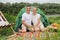 Smiling happy optimistic woman and man wearing casual clothing sitting at tent near the river looking at camera having picnic