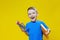 Smiling happy schooler in blue t-shirt holding multicolored pencils and book on yellow background