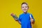 Smiling happy schooler in blue t-shirt holding multicolored pencils and book on yellow background