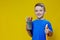 Smiling happy schooler in blue t-shirt holding multicolored pencils and book on yellow background