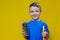 Smiling happy schooler in blue t-shirt holding multicolored pencils and book on yellow background