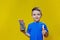 Smiling happy schooler in blue t-shirt holding multicolored pencils and book on yellow background