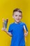 Smiling happy schooler in blue t-shirt holding multicolored pencils and book on yellow background