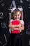 Smiling happy schoolgirl standing before the chalkboard as a background with a couple of books hugging them. Portrait