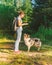 Smiling happy woman in casual clothes playing with dog in park on summer day