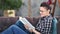 Smiling hipster young girl wearing glasses reading book sitting on couch at home medium shot