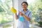 Smiling Hispanic charming woman maid, housewife sprays glass cleaner detergent on yellow cloth during spring cleaning