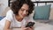 Smiling hispanic curly woman student uses smartphone tapping screen display