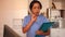 Smiling Hispanic woman doctor in blue uniform standing in clinic, filling out clipboard with medical records