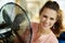 Smiling housewife cooling down using electric metallic fan