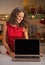 Smiling housewife looking on laptop blank screen in kitchen