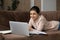 Smiling Indian woman in earphones studying online, lying on couch